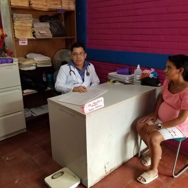 A pregnant woman sitting at a desk talking to a doctor.