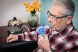 Elderly man using a breathing treatment machine.