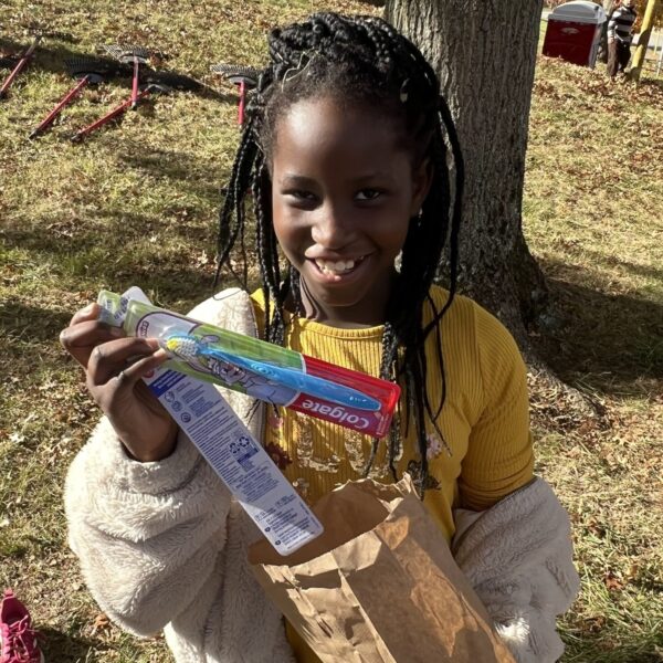 A young girl smiling and holding toothbrushes.