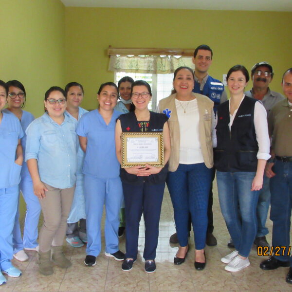 Miembros del personal del hospital en batas de pie en un grupo con nuestra Directora Ejecutiva, Ángela García, en el medio sosteniendo una placa.