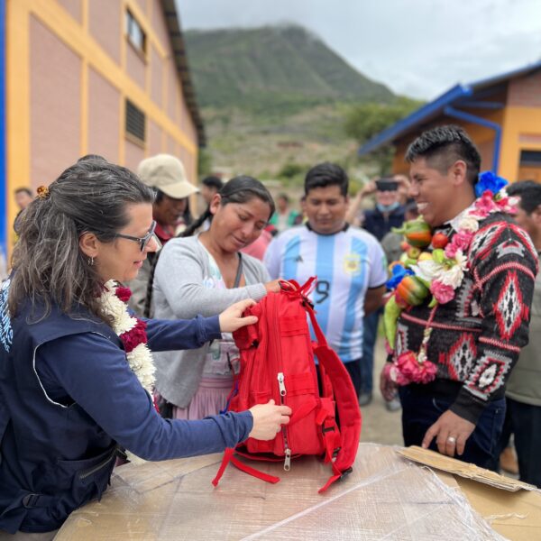 Un grupo de hombres y mujeres parados alrededor de una mesa con una mochila roja en el medio. Directora Ejecutiva, Ángela García, mostrando a todos el contenido de la mochila.