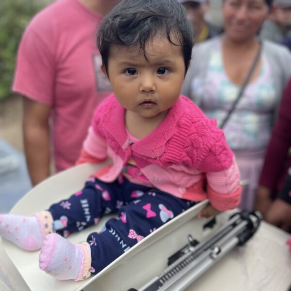 A baby wearing pink and purple sitting on a baby scale.