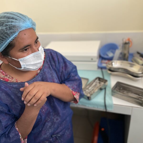 Una enfermera con batas y mascarilla de pie frente a los suministros médicos.